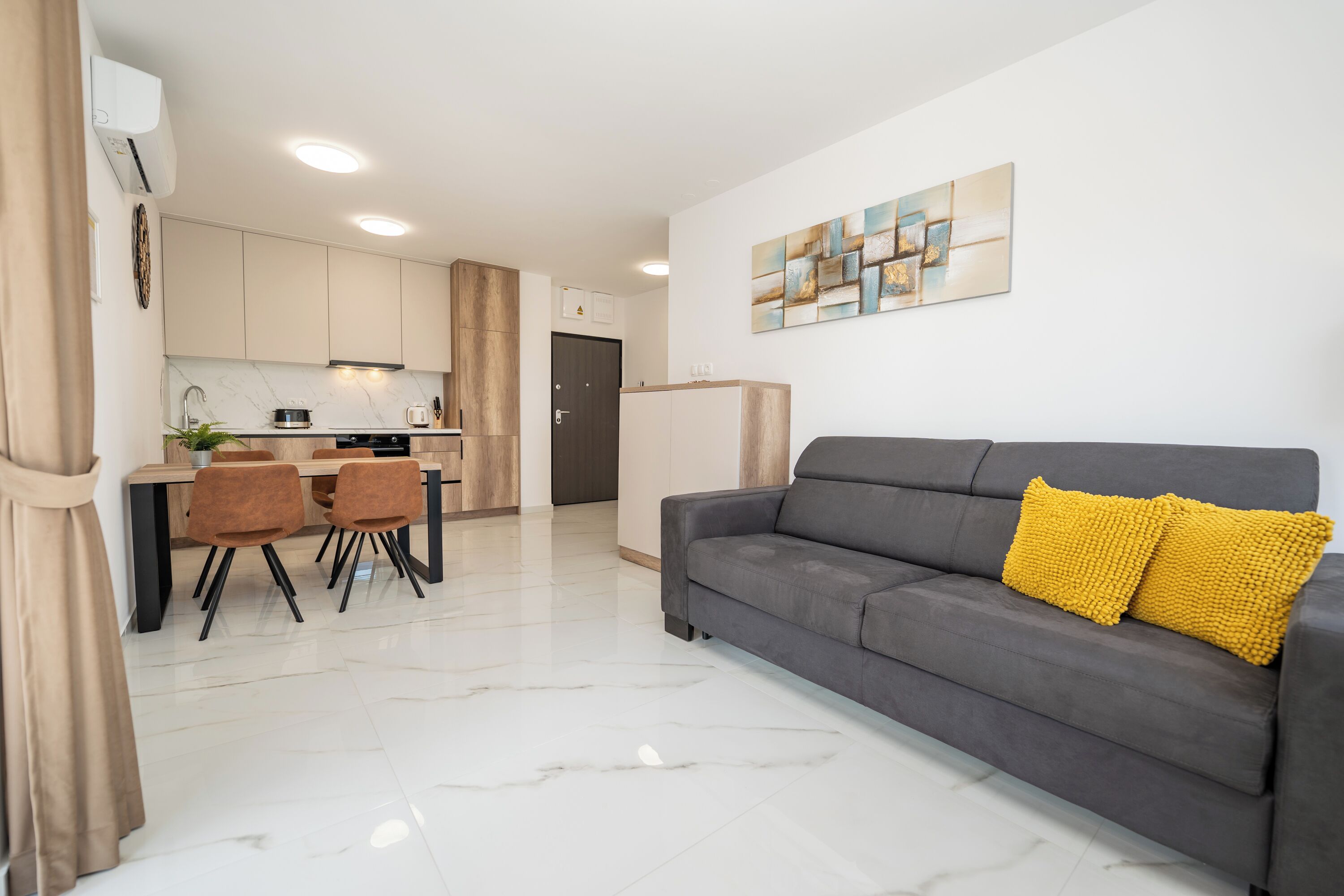 A modern living room with a grey sofa, a yellow throw pillow, and a dining area with a table and chairs.