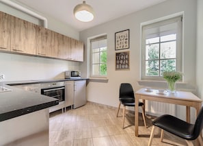 A modern kitchen with wooden cabinets, a built-in oven, a microwave, and a dining area with a table and chairs. - Imperial Apartments - Patio Mare (Sopot)