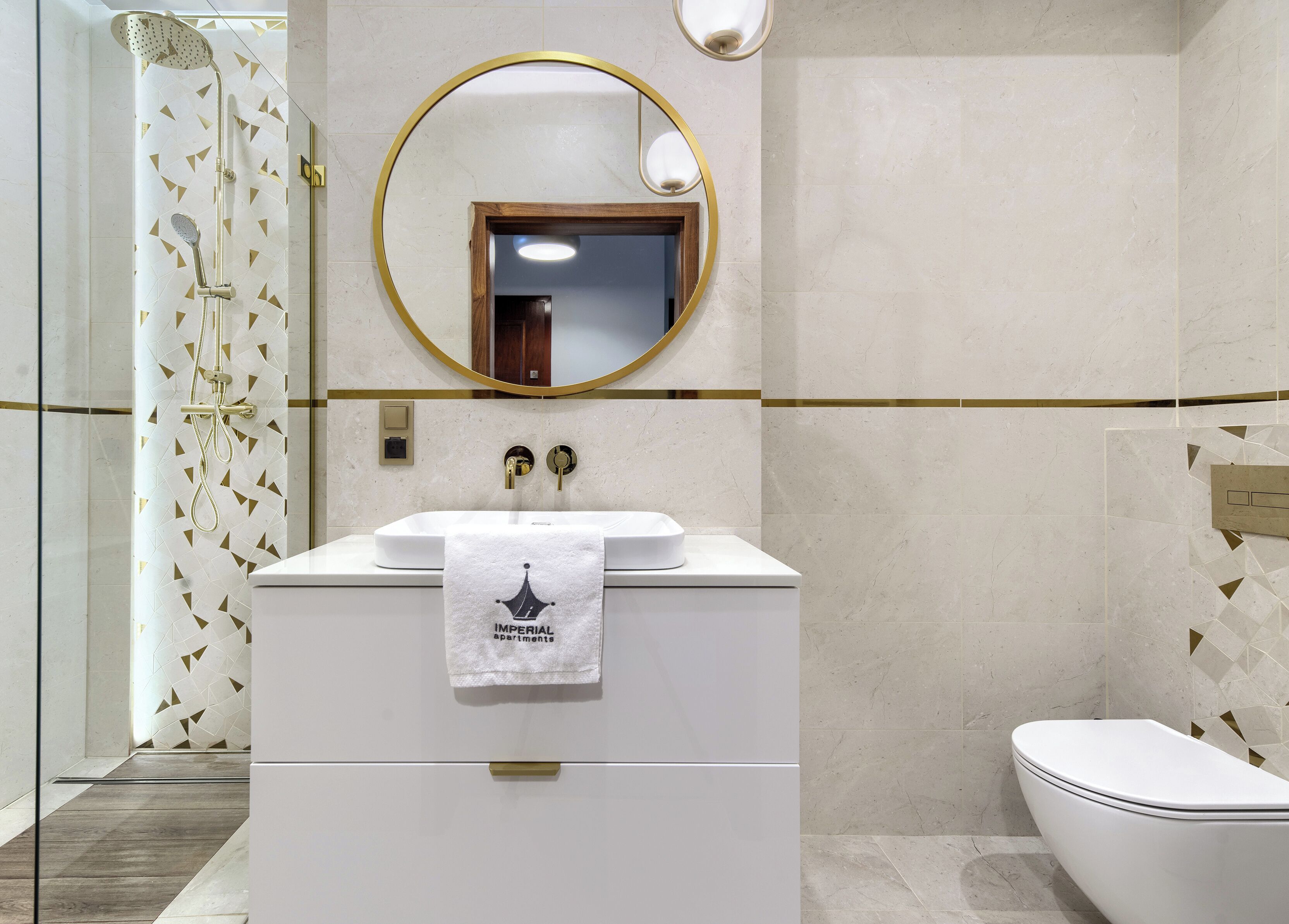 Ein modernes Badezimmer mit einem weißen Waschtisch, einem goldfarbenen Spiegel und einer Dusche mit geometrischem Fliesenmuster.