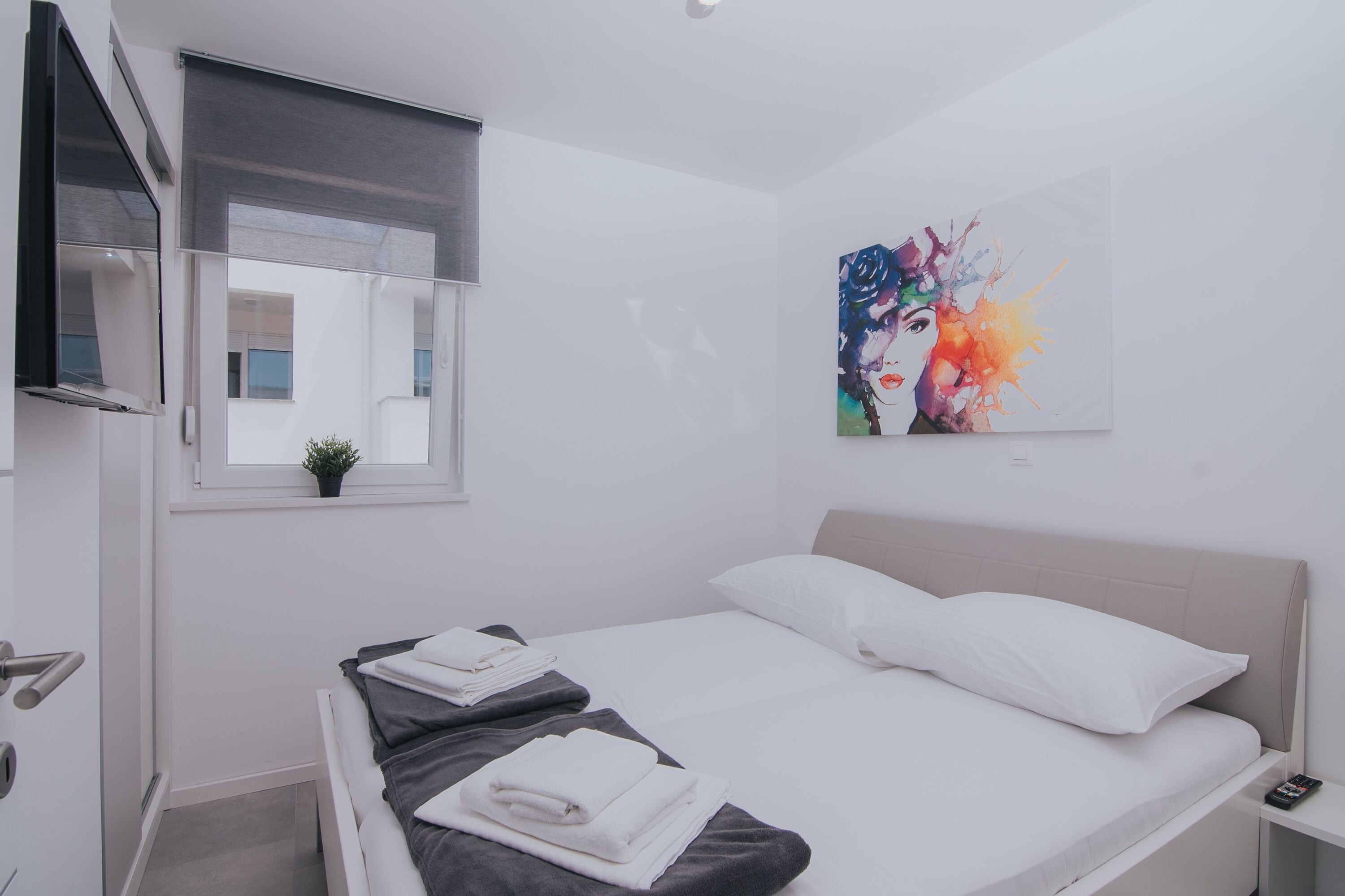 A modern bedroom with a bed, a bedside table, a window with a view, and a painting on the wall.