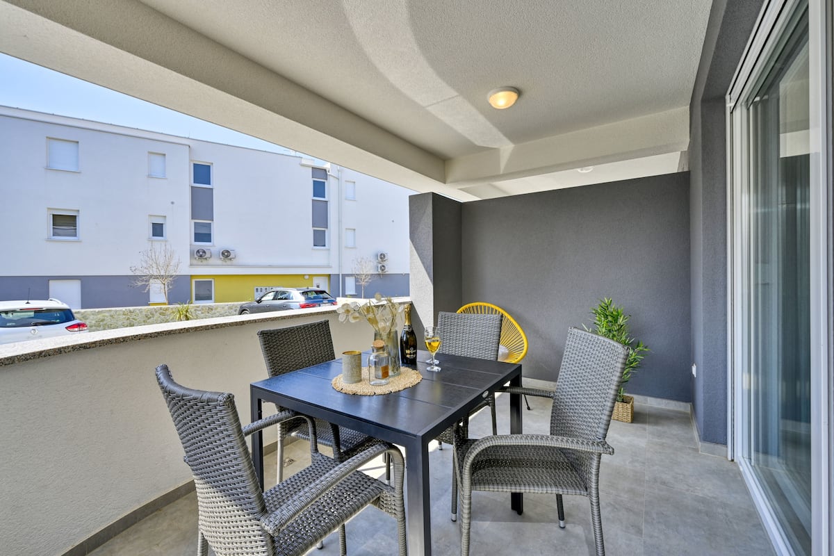 A balcony with a table and chairs, a potted plant, and a view of a building in the background.