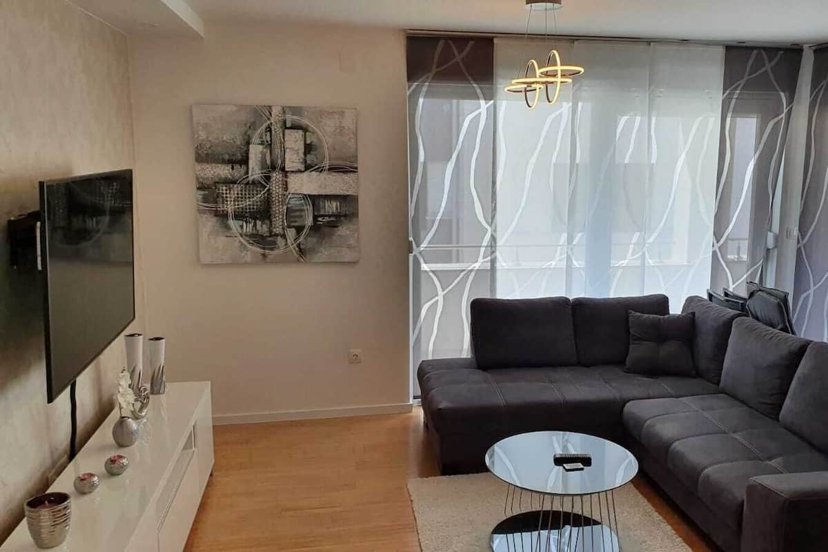 A modern living room with a sectional sofa, a flat-screen TV, and a decorative wall piece.