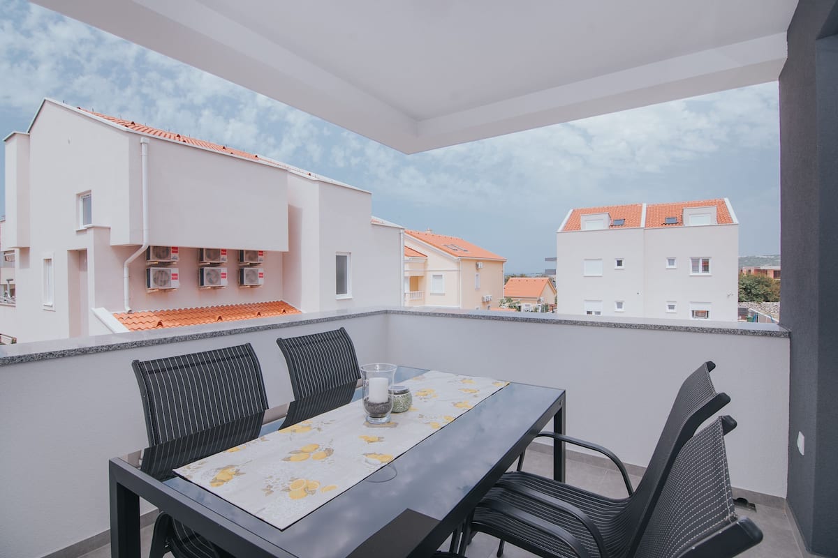 A balcony with a table and chairs, overlooking a residential area with buildings.
