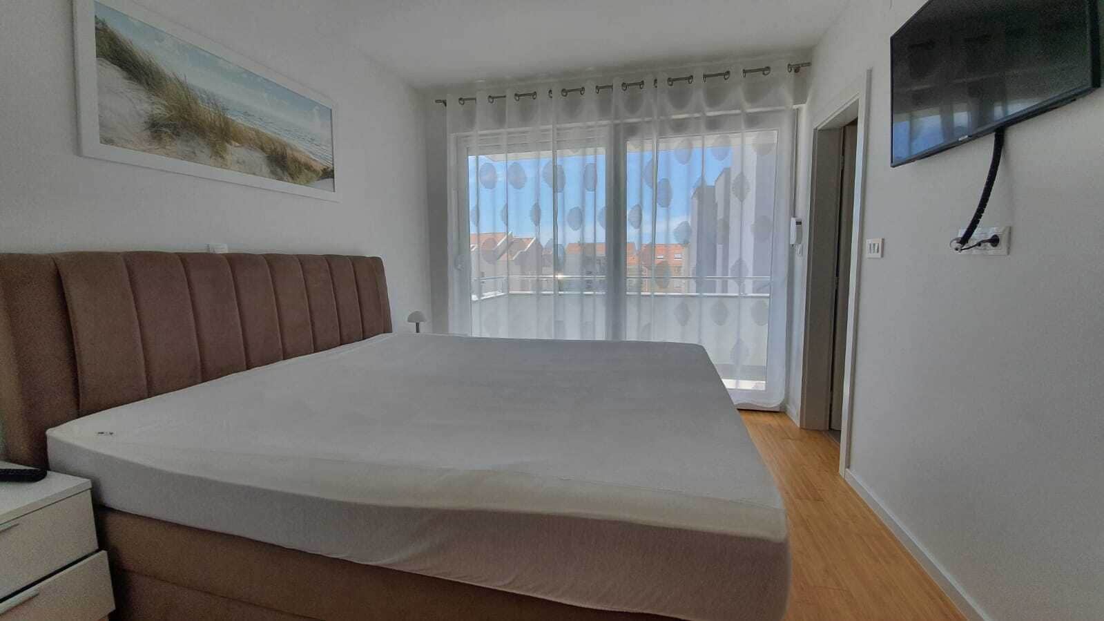 Un dormitorio con cama, televisor montado en la pared y ventana con cortinas.