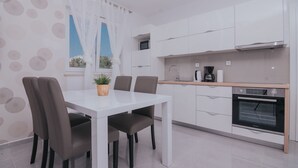 Een moderne keuken met witte kasten, een inbouwoven en een eethoek met een witte tafel en stoelen.