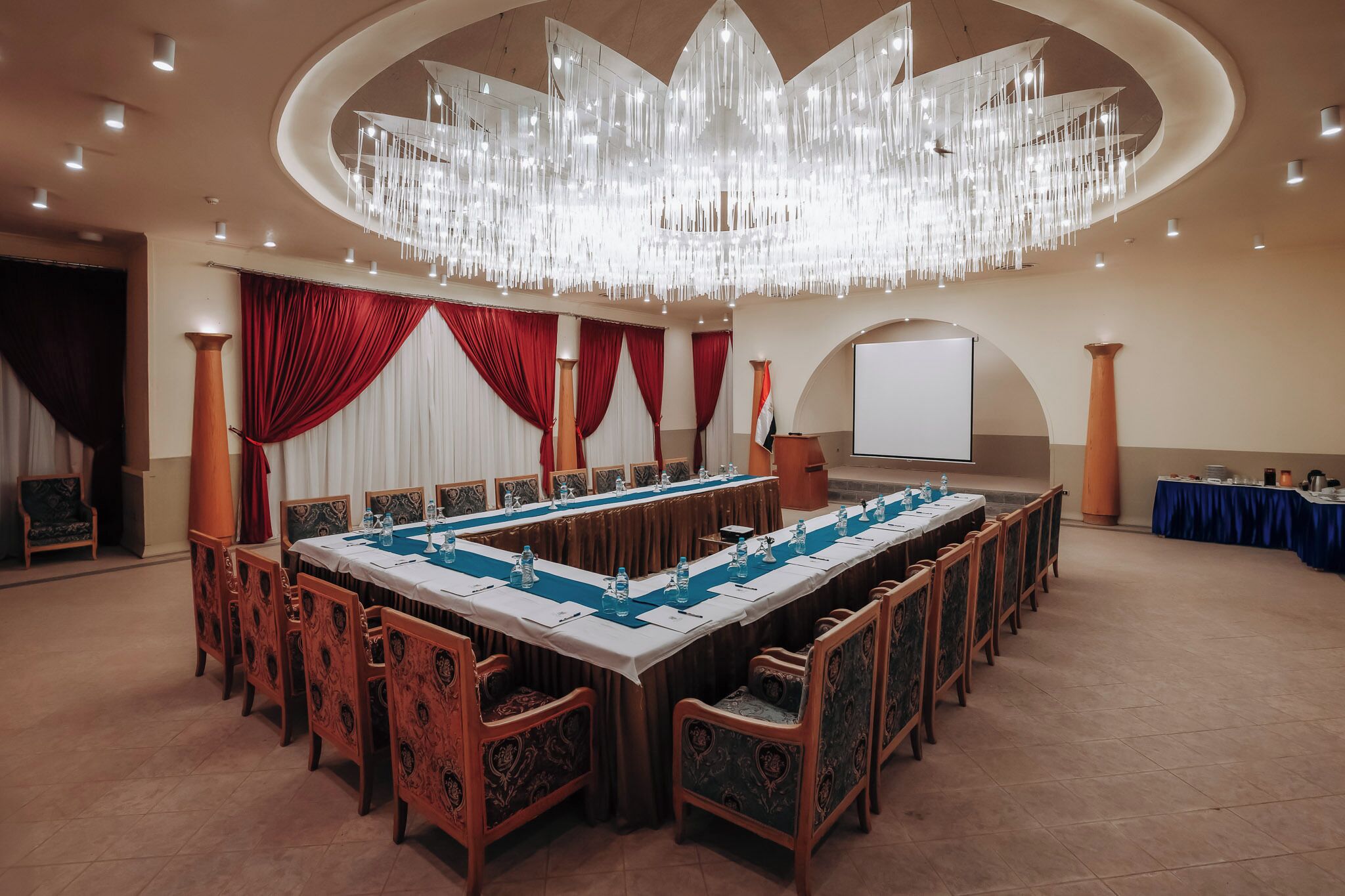 A conference room with a long table, chairs, a projector screen, and a chandelier.