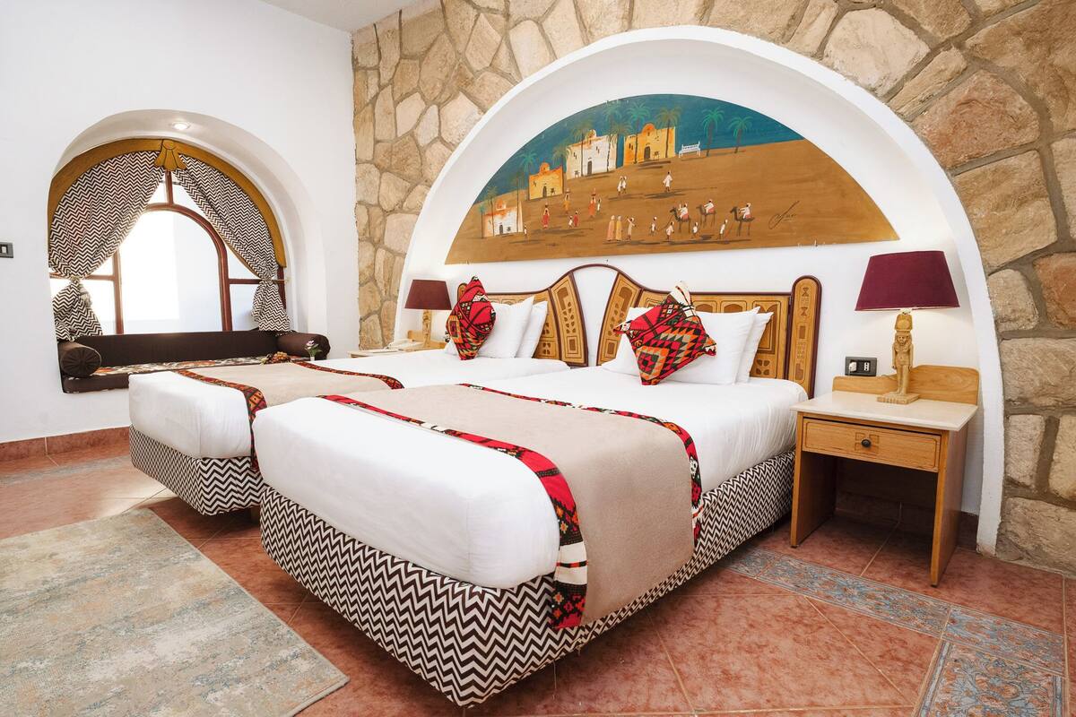 A hotel room with a large bed, two bedside tables, a nightstand, a decorative archway, and a mural on the wall.