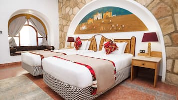 Una habitación de hotel con una cama grande, dos mesitas de noche, un mueble auxiliar y un arco decorativo, además de un mural en la pared.