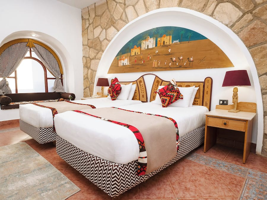 Una habitación de hotel con una cama grande, dos mesitas de noche, un mueble auxiliar y un arco decorativo, además de un mural en la pared.