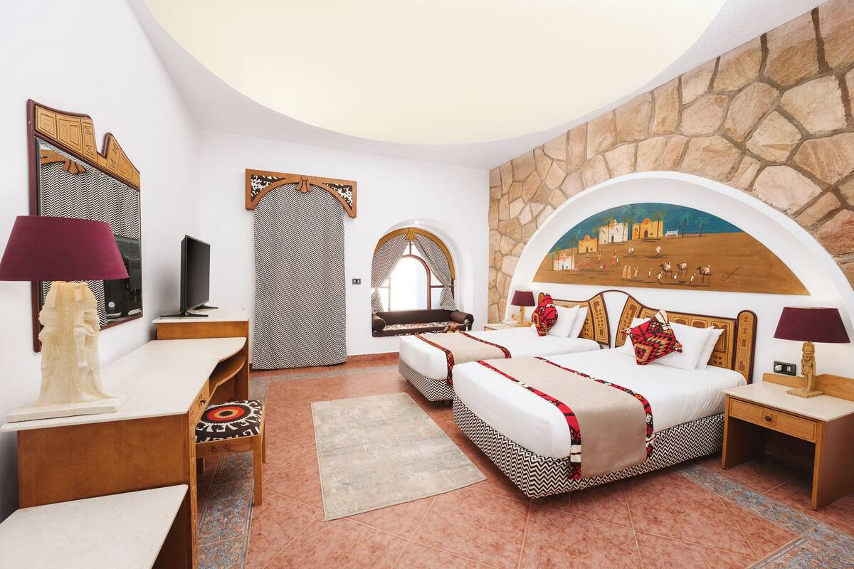 A hotel room with a large bed, a desk, a chair, a TV, and a stone wall mural.