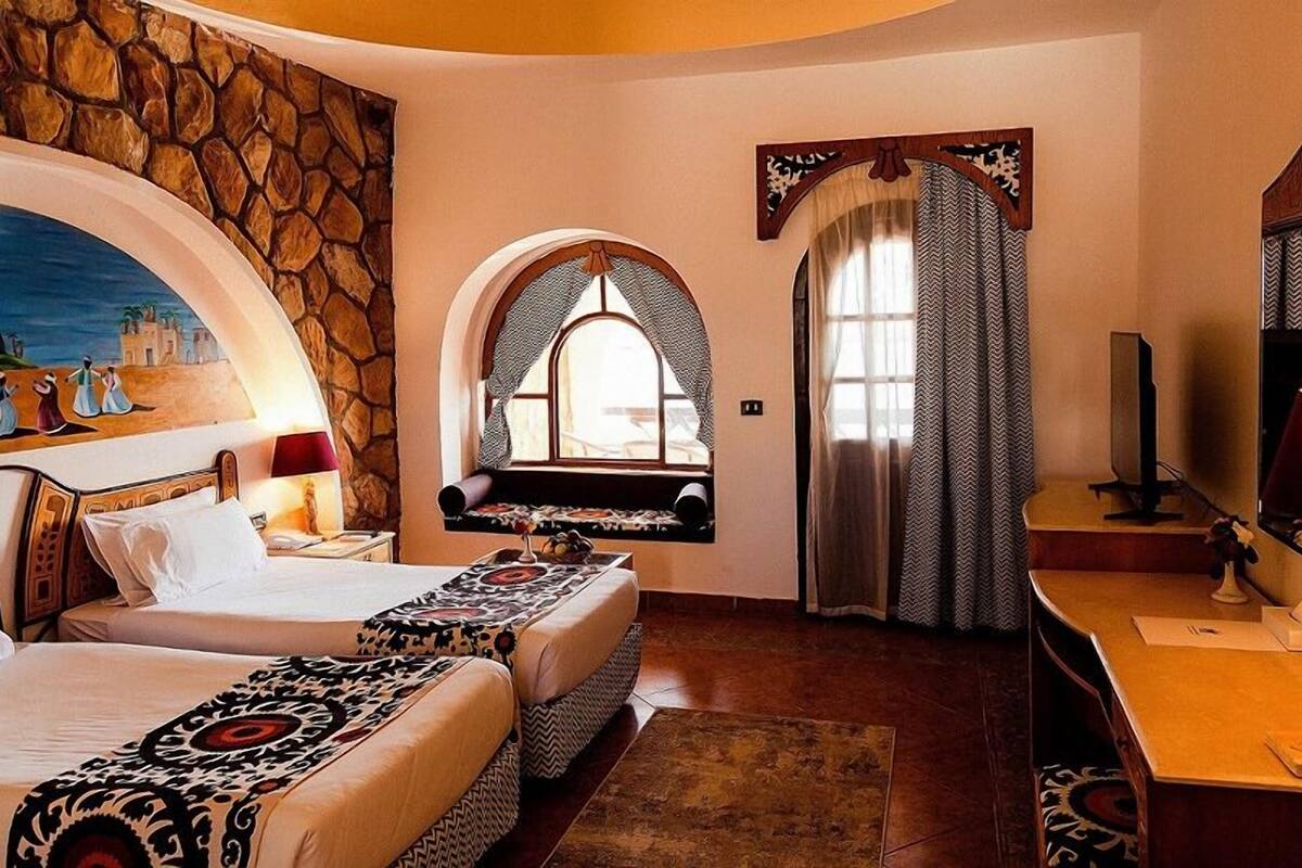 A room with two beds, a stone wall, a mural, a window with a view, and a television.