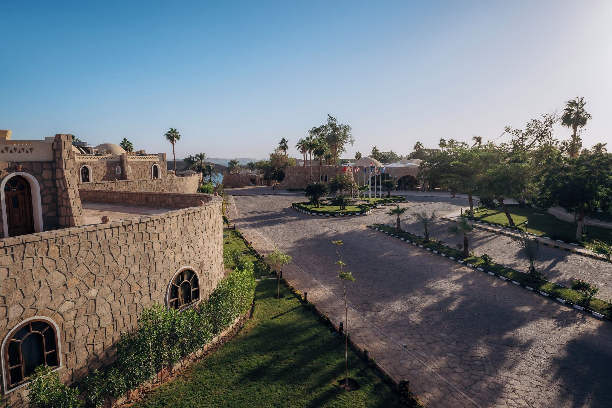 A courtyard with stone buildings, palm trees, and a central garden area.
