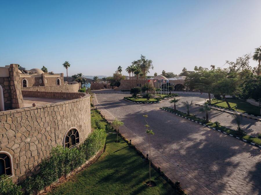 A courtyard with stone buildings, palm trees, and a central garden area.