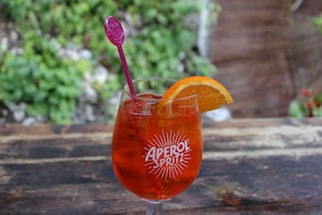 Ett glas Aperol Spritz med en apelsinskiva och ett lila sugrör, placerat på en träyta.