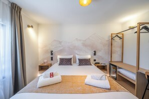 Habitación de hotel con cama, mesita de noche, armario y un espejo, y una pared decorada con un mural de montañas.