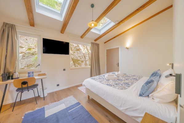 Un dormitorio con cama, escritorio, silla, televisor y tragaluz.