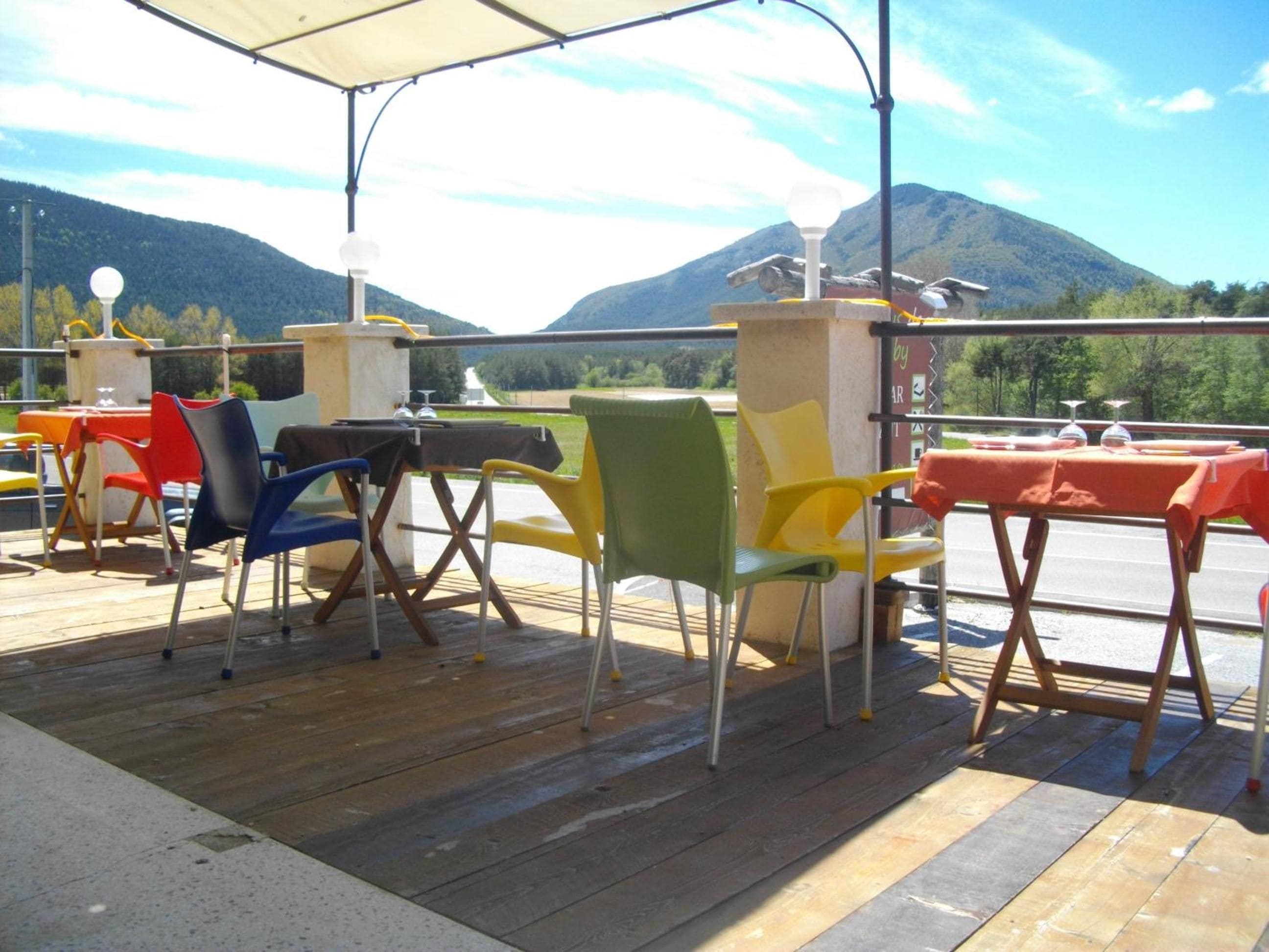 An outdoor seating area with chairs and tables, a wooden deck, and a mountain view in the background.