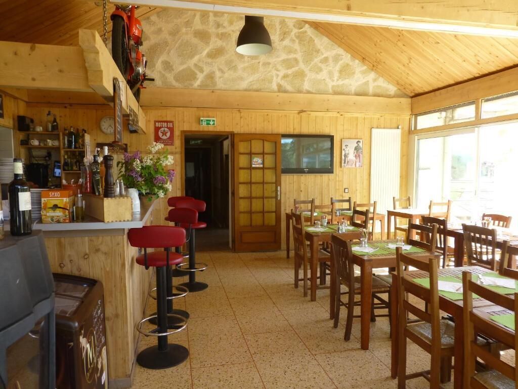 A restaurant with wooden walls and a stone ceiling, featuring a bar area with stools and a dining area with tables and chairs.