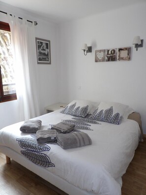 Una cama bien hecha con almohadas y toallas, una pared con un cartel que dice 'LOVE', y una ventana con cortinas.