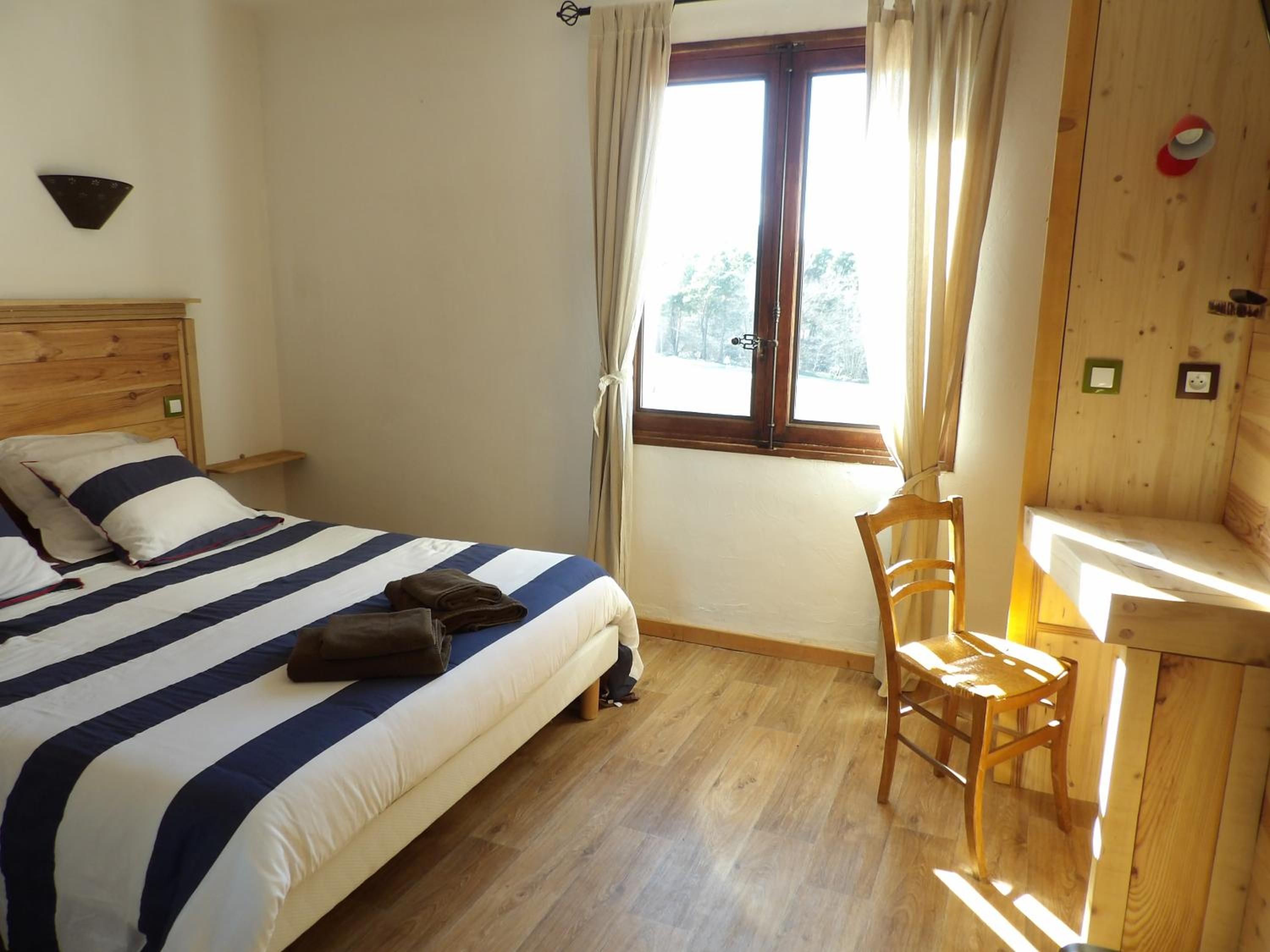 A bedroom with a bed, a chair, a window, and a wooden wall.