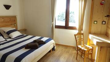 A bedroom with a bed, a chair, a window, and a wooden wall.