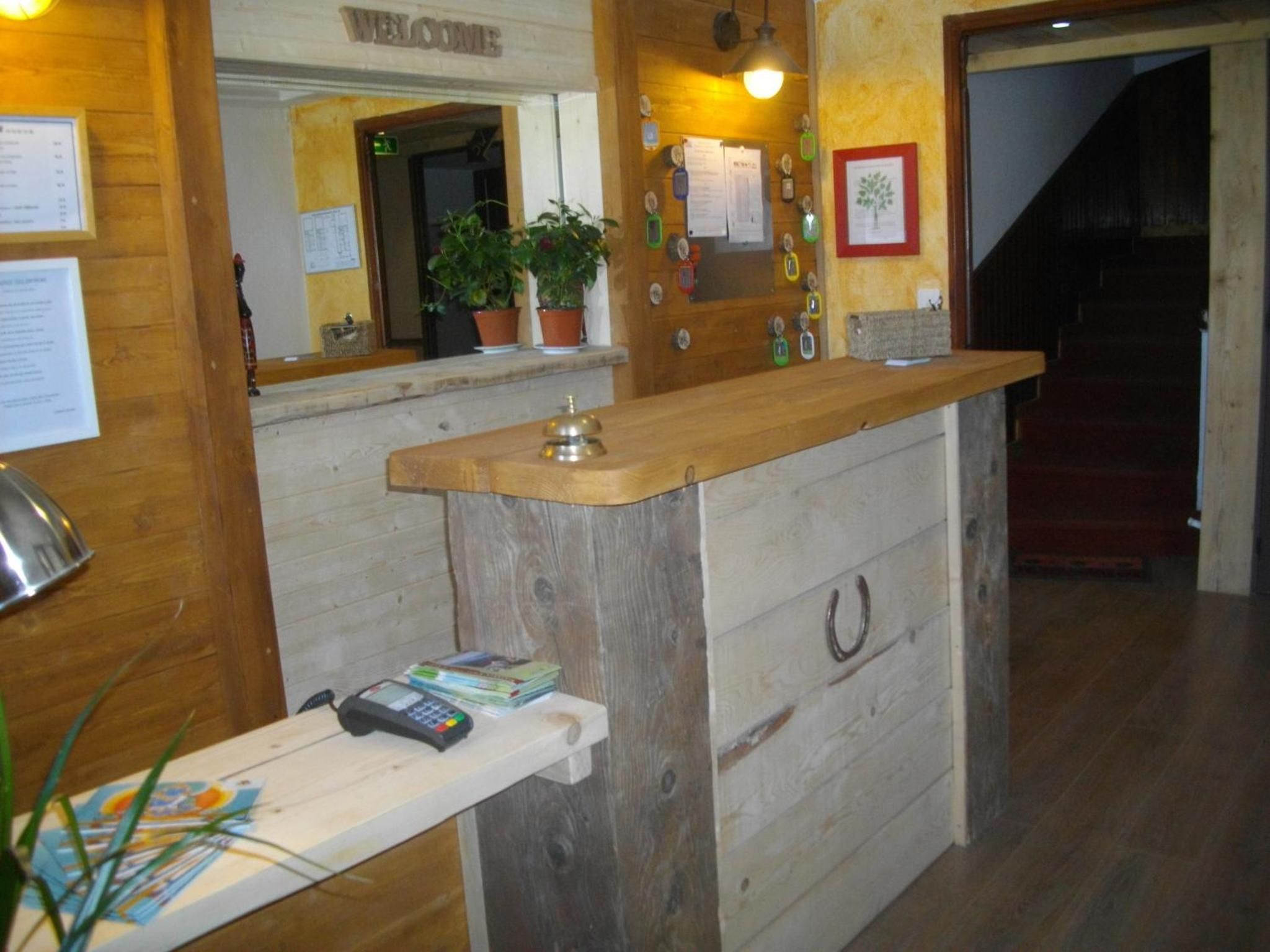 Een receptiebalie met een houten toonbank, een kassa, een telefoon en een klein plankje met boeken.
