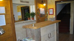 Un mostrador de recepción con una encimera de madera, una caja registradora, un teléfono y un estante pequeño con libros.