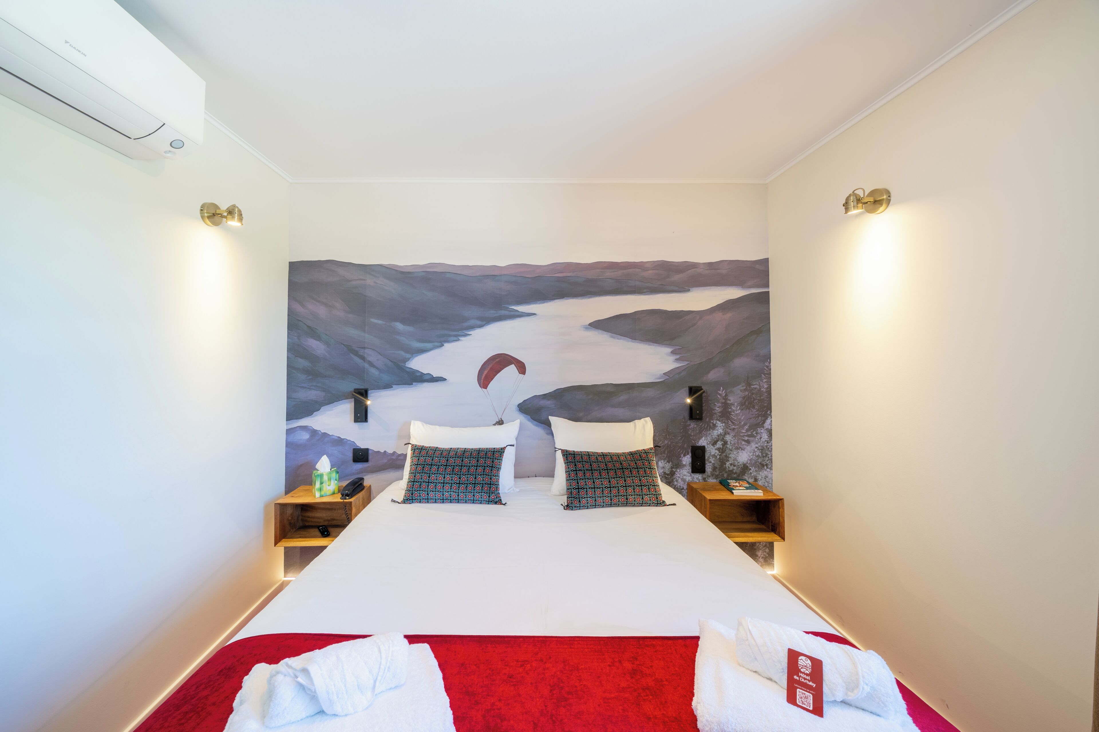 Habitació d'hotel amb un llit gran, dues taules de nit, una làmpada penjada a la paret i un quadre de paisatge.