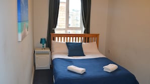 A neatly made bed with a blue bedspread and white pillows, a wooden headboard, and a small bedside table with a lamp. - Abbey Street City Centre Apartment (Dublin)