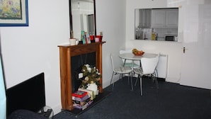 A room with a fireplace, a dining table with chairs, a kitchen area with cabinets, and a framed picture on the wall. - Abbey Street City Centre Apartment (Dublin)
