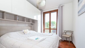 A neatly made bed with a white duvet and a pillow, a chair, and a window with curtains. - My Sirmione Beach Apartment Superior (Sirmione)