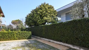 A garden with a paved walkway, a tall hedge, and a tree. - My Sirmione Beach Apartment Superior (Sirmione)