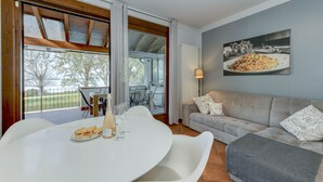 A dining area with a table set for two, a sofa, and a large window with curtains. - My Sirmione Beach Apartment Superior (Sirmione)