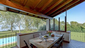 An outdoor dining area with a wooden table set for four, overlooking a swimming pool and lush greenery. - My Sirmione Beach Apartment Superior (Sirmione)