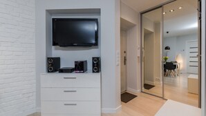 Un salon moderne doté d’un téléviseur à écran plat, de haut-parleurs intégrés et d’un meuble de rangement blanc pour les appareils multimédias.
