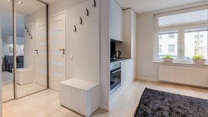 Un appartement moderne doté d’une kitchenette, d’une grande fenêtre avec stores et d’un tapis noir sur le sol.