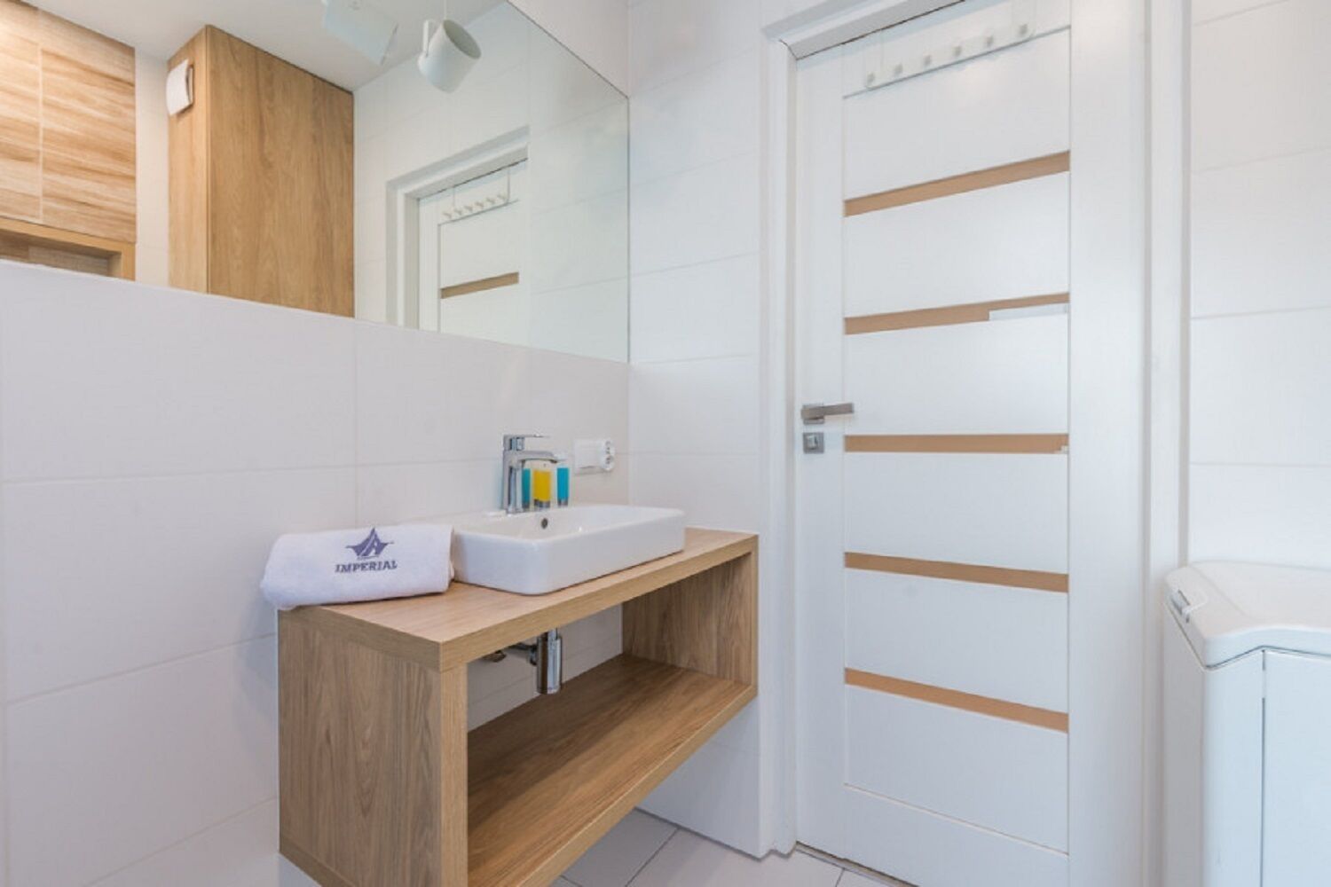 Een moderne badkamer met een houten wastafelmeubel, een witte wasbak en een grote spiegel.