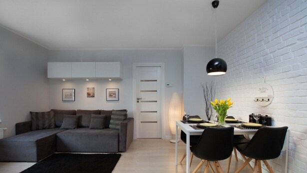 Un salon moderne avec un canapé gris, une table à manger avec des chaises et un mur en briques blanches.