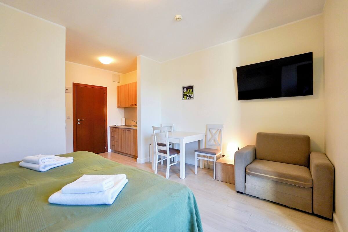 Habitación de hotel con cama, sofá, televisión, una mesita y una silla.