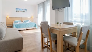 A hotel room with a bed, a TV, a dining table with chairs, and a sofa.