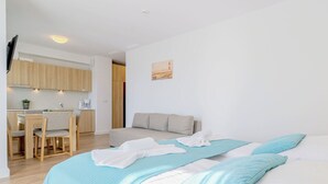 A modern hotel room with a bed, a sofa, a dining area, and a kitchen.