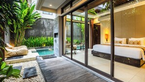 A modern bedroom with a large bed, a glass door leading to a pool, and a patio area with seating and plants. - La Paradis Villa (Pererenan)