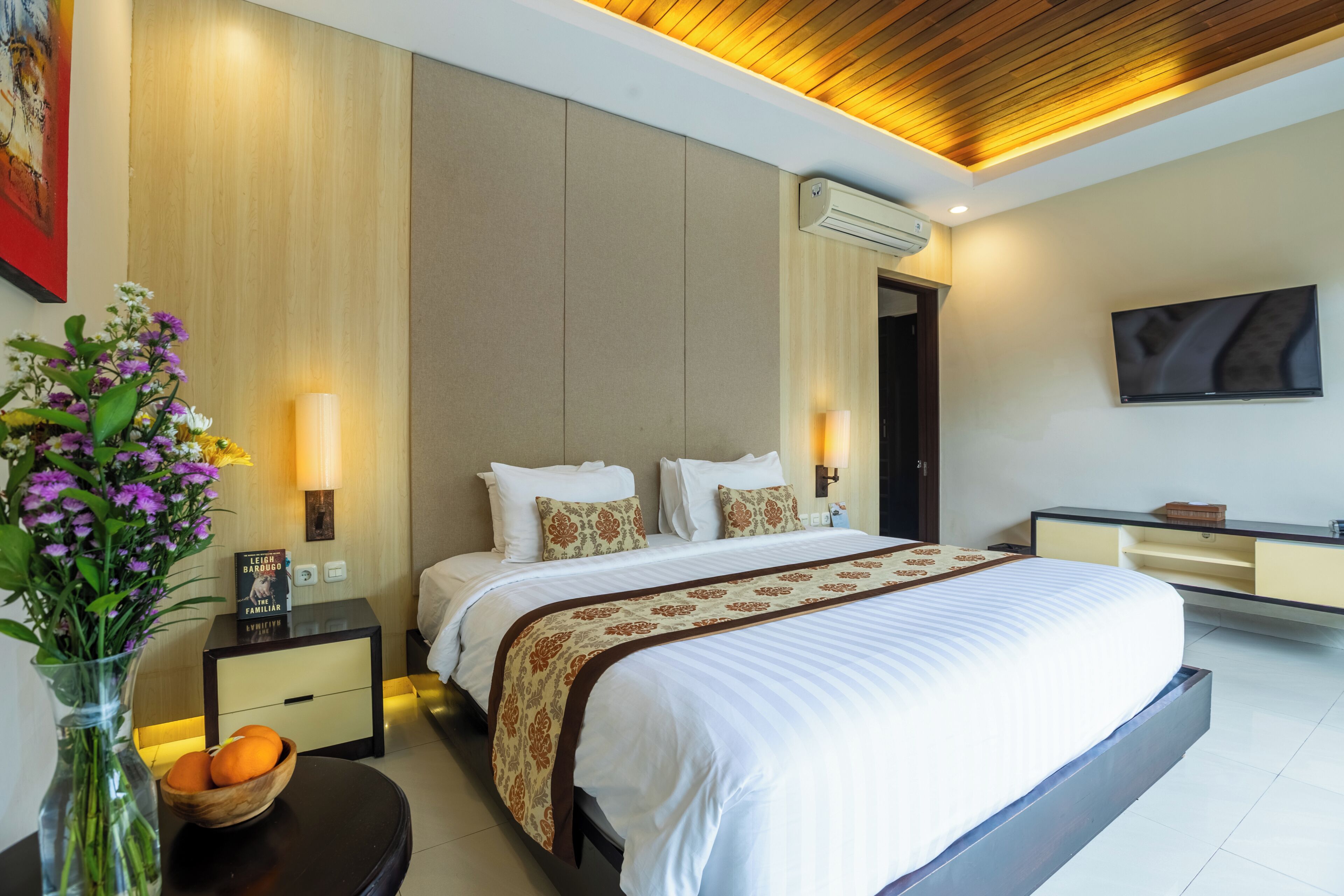 Una habitación de hotel moderna con una cama grande, mesitas de noche, un televisor y un jarrón con flores.