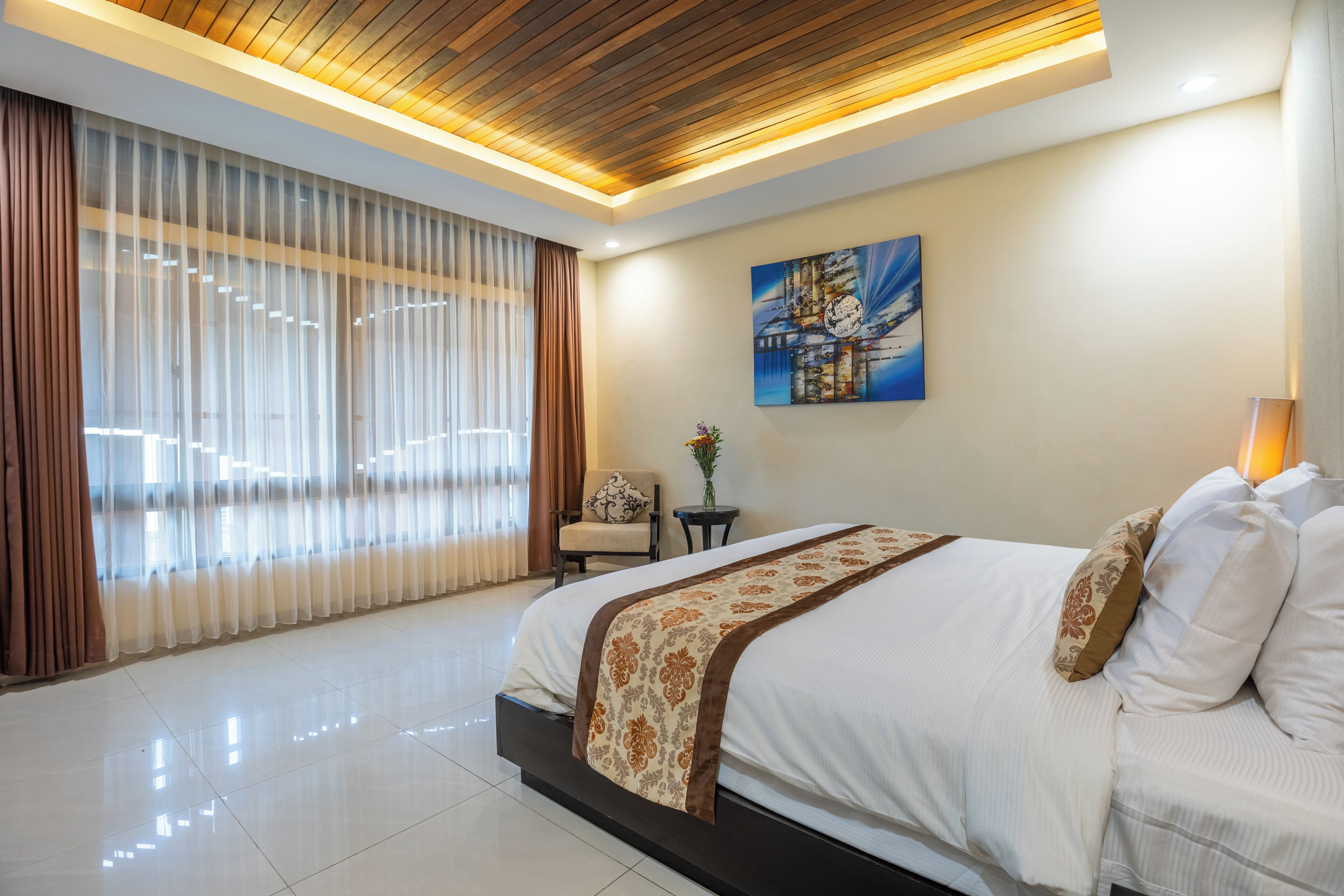 Une chambre d’hôtel moderne avec un grand lit, un tableau au mur et une vue à travers des rideaux transparents.