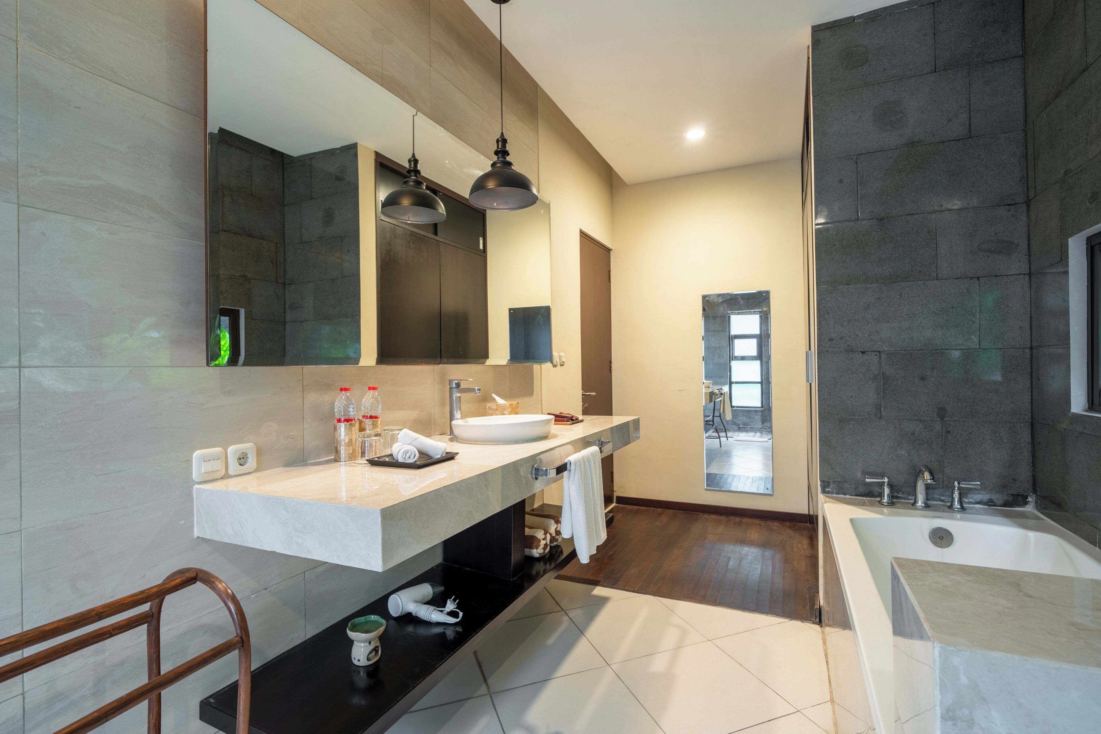 Une salle de bain moderne avec un grand miroir, deux lampes suspendues, une baignoire et un meuble-lavabo avec un évier.