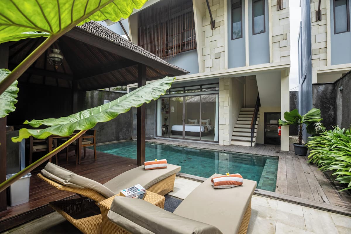 A pool area with lounge chairs, a covered seating area, and a staircase leading to a bedroom.
