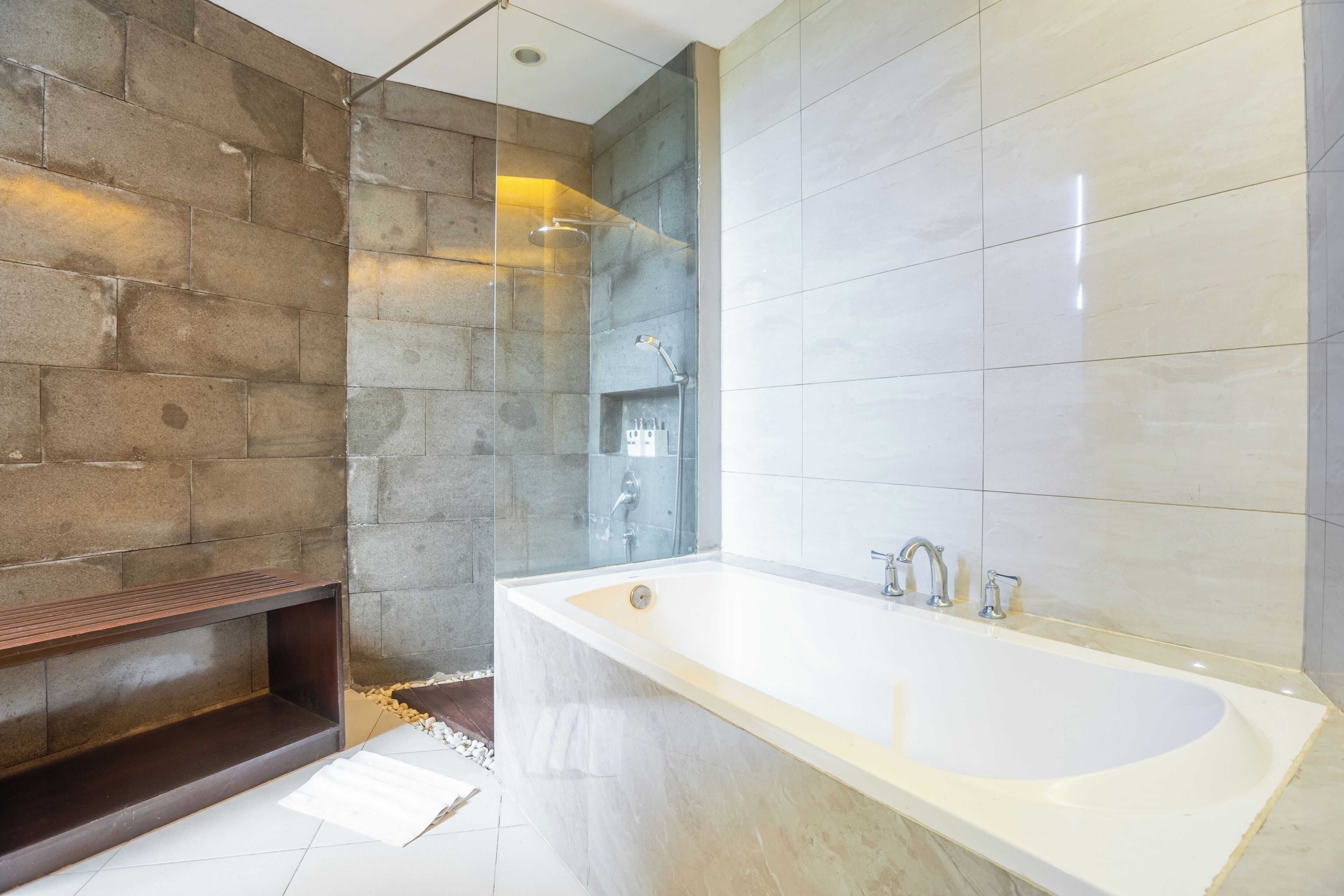 A modern bathroom with a large bathtub, a glass-enclosed shower, and a wooden bench.