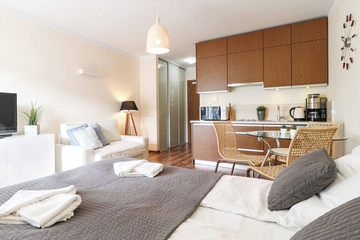 A modern hotel room with a bed, a small kitchenette, a dining area, and a TV.