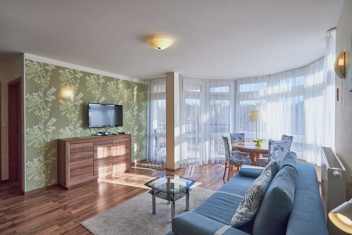 A modern living room with a sofa, a glass coffee table, a TV on a wooden cabinet, and a dining area with a table and chairs.