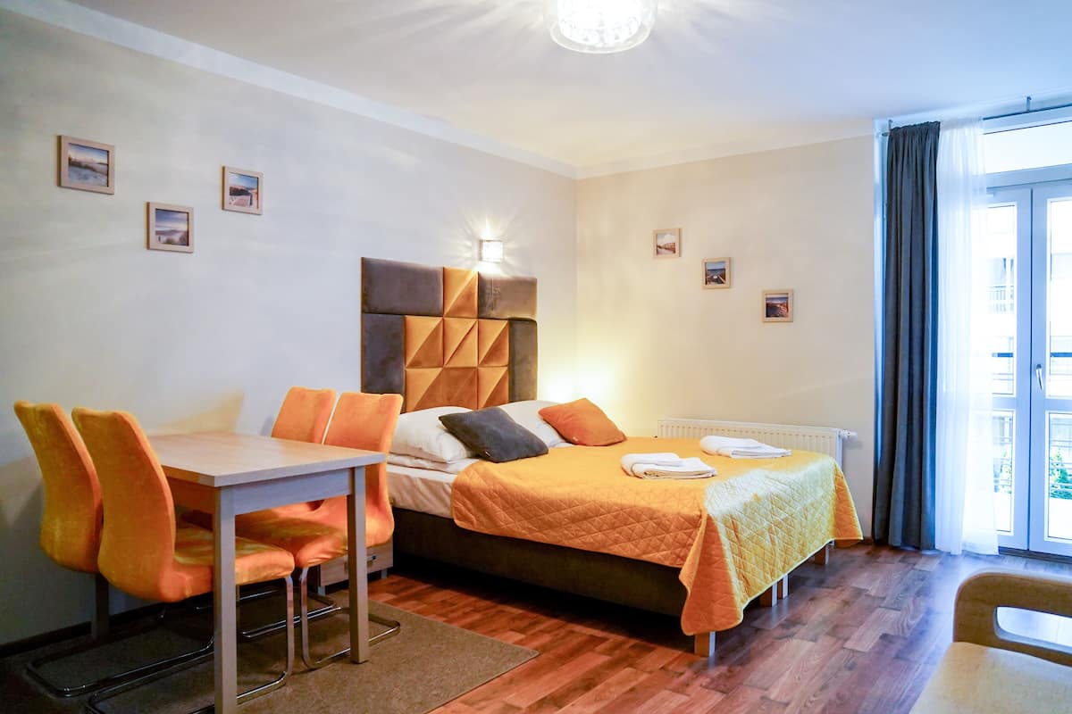 A hotel room with a bed, a table, and chairs, a window with curtains, and a radiator.